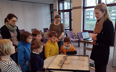 Eine Gruppe von Grundschulkindern steht vor einer mittelalterlichen Urkunde im Lesesaal des NLA in Oldenburg.