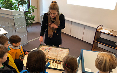 Eine Gruppe von Grundschulkindern steht vor einer mittelalterlichen Urkunde im Lesesaal des NLA in Oldenburg.