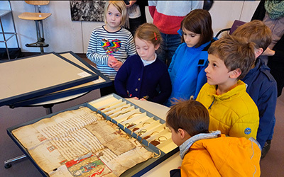 Eine Gruppe von Grundschulkindern steht vor einer mittelalterlichen Urkunde im Lesesaal des NLA in Oldenburg.